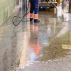 A worker for an industrial cleaning company power washing floor.